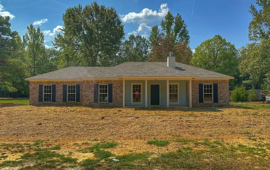 Long brick ranch home with black shutters and a covered front porch on a wooded lot