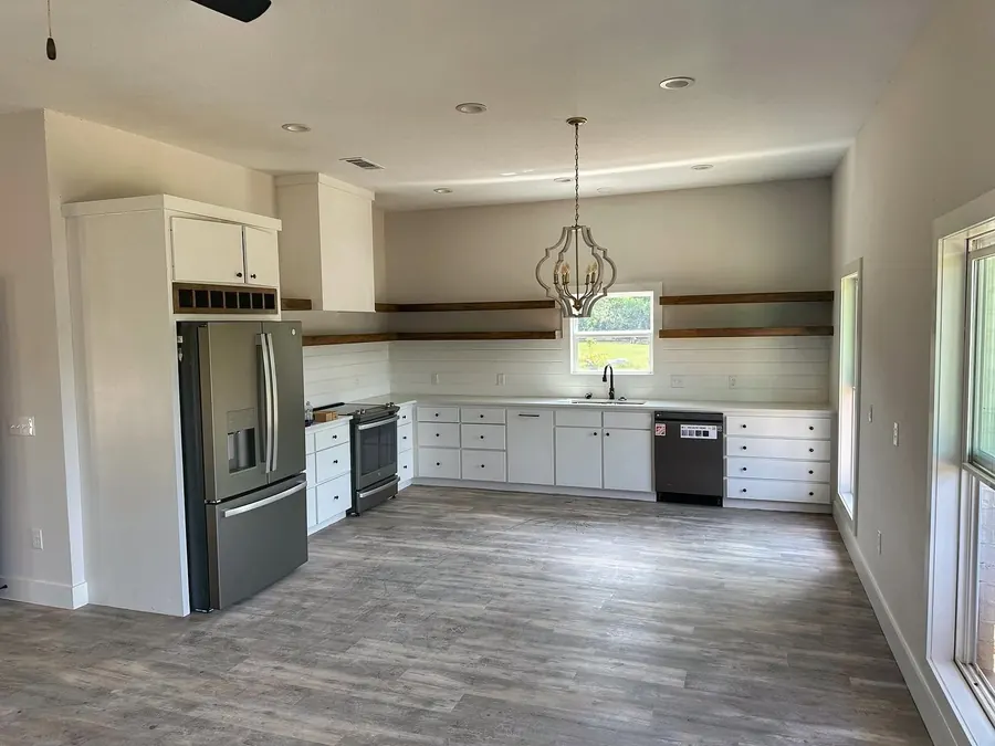 Open kitchen with white cabinets, floating wood shelves and a pendant light