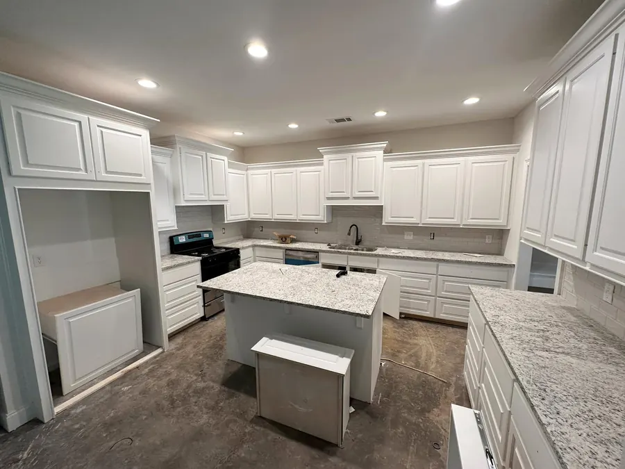 White custom kitchen with an island, granite counters and recessed lighting