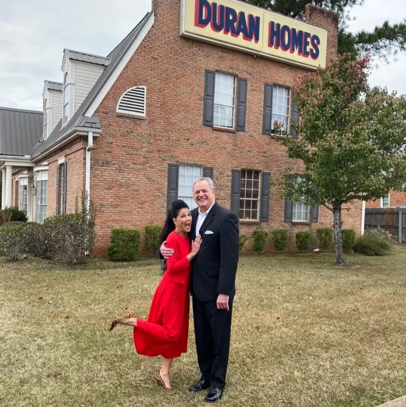 Two members of the Duran family smiling on the lawn in front of the brick Duran Homes office and its sign